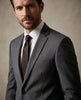Man wearing a gray suit with a brown tie against a neutral background