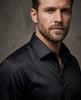 Man wearing a black dress shirt against a gray background
