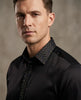 Man wearing a black shirt with a patterned collar against a neutral background