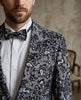 Man wearing a patterned suit jacket with a bow tie against a neutral background