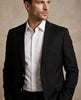 Man wearing a black suit jacket over a white shirt against a beige background