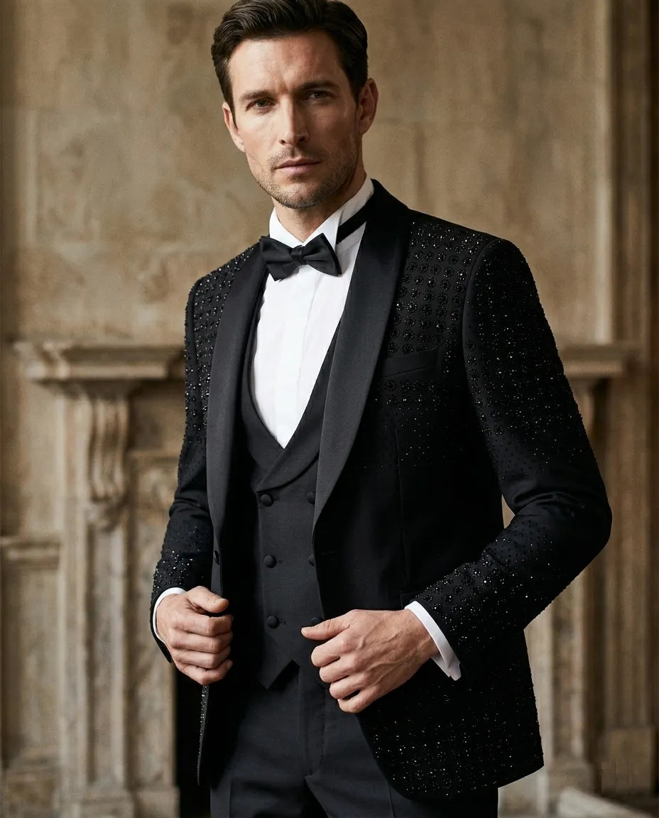Man wearing a black tuxedo with a bow tie against a stone wall background