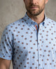 Man wearing a blue short-sleeve shirt with brown pattern against a neutral background