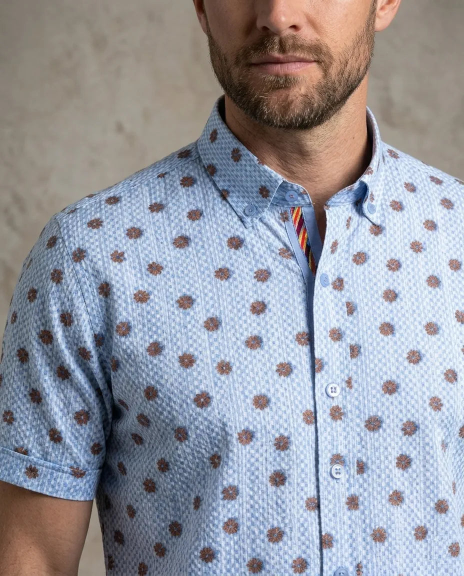 Man wearing a blue short-sleeve shirt with brown pattern against a neutral background