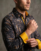 Man wearing a patterned shirt with yellow accents against a gray background