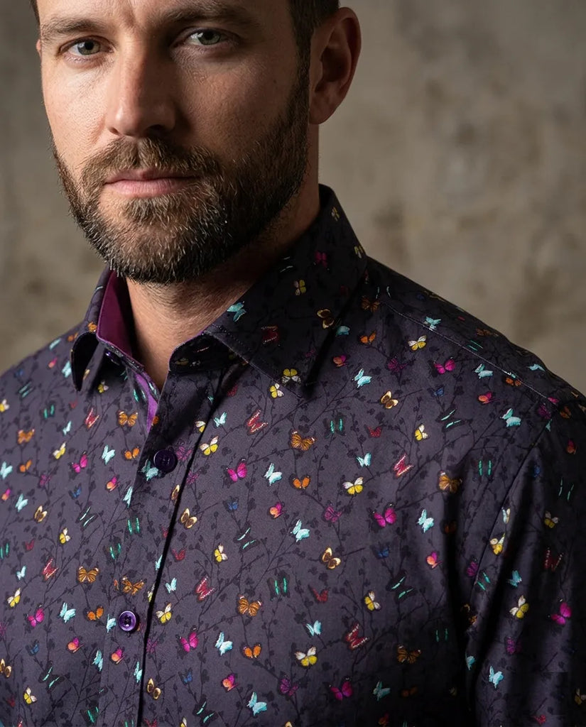 Man wearing a dark shirt with colorful butterfly pattern against a neutral background
