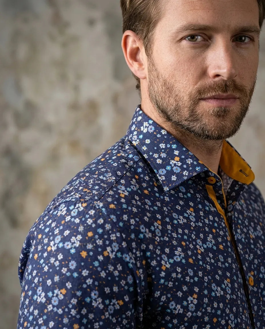 Man wearing a navy blue floral shirt with a blurred concrete wall background