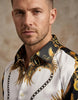Man wearing a white shirt with gold and black patterned collar against a beige background