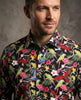 Man wearing a colorful tropical shirt with parrot and floral pattern against a neutral background