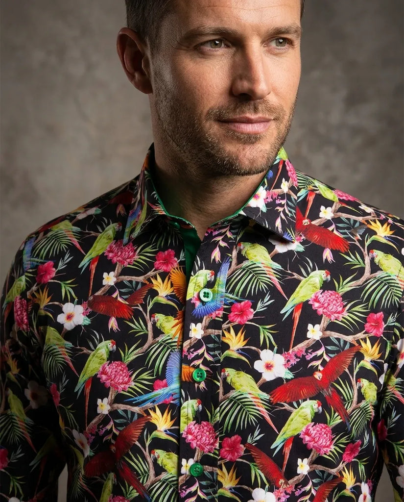 Man wearing a colorful tropical shirt with parrot and floral pattern against a neutral background