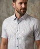 Man wearing a short-sleeve shirt with a colorful pattern against a textured wall.