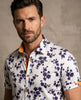Man wearing a white floral shirt with orange accents against a beige background