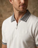 Man wearing a white polo shirt with a patterned collar against a beige background