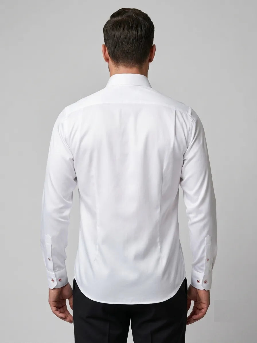 A man viewed from the back wearing a white long-sleeve dress shirt and black trousers, standing against a plain light gray studio background.